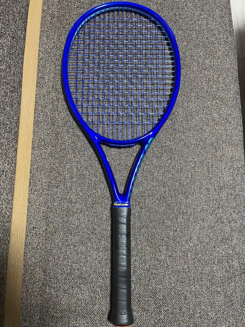 Blue Wilson Ultra Tour 98J tennis racket shown full-length on a carpeted floor.