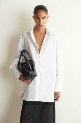 Woman modeling the wing-collar cotton tuxedo shirt, holding a black handbag and wearing a sheer black skirt.