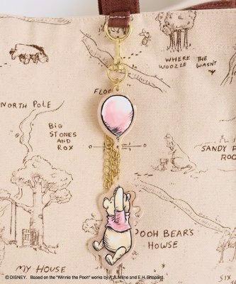 Winnie the Pooh bag charm with a Pooh figure holding a pink balloon, attached by a chain to a beige canvas bag.