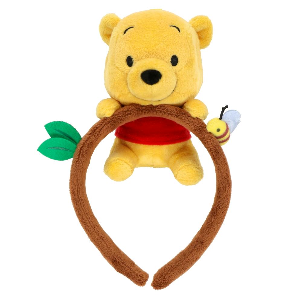 A brown plush headband topped with a small Winnie the Pooh plush, a green leaf, and a bee decoration.