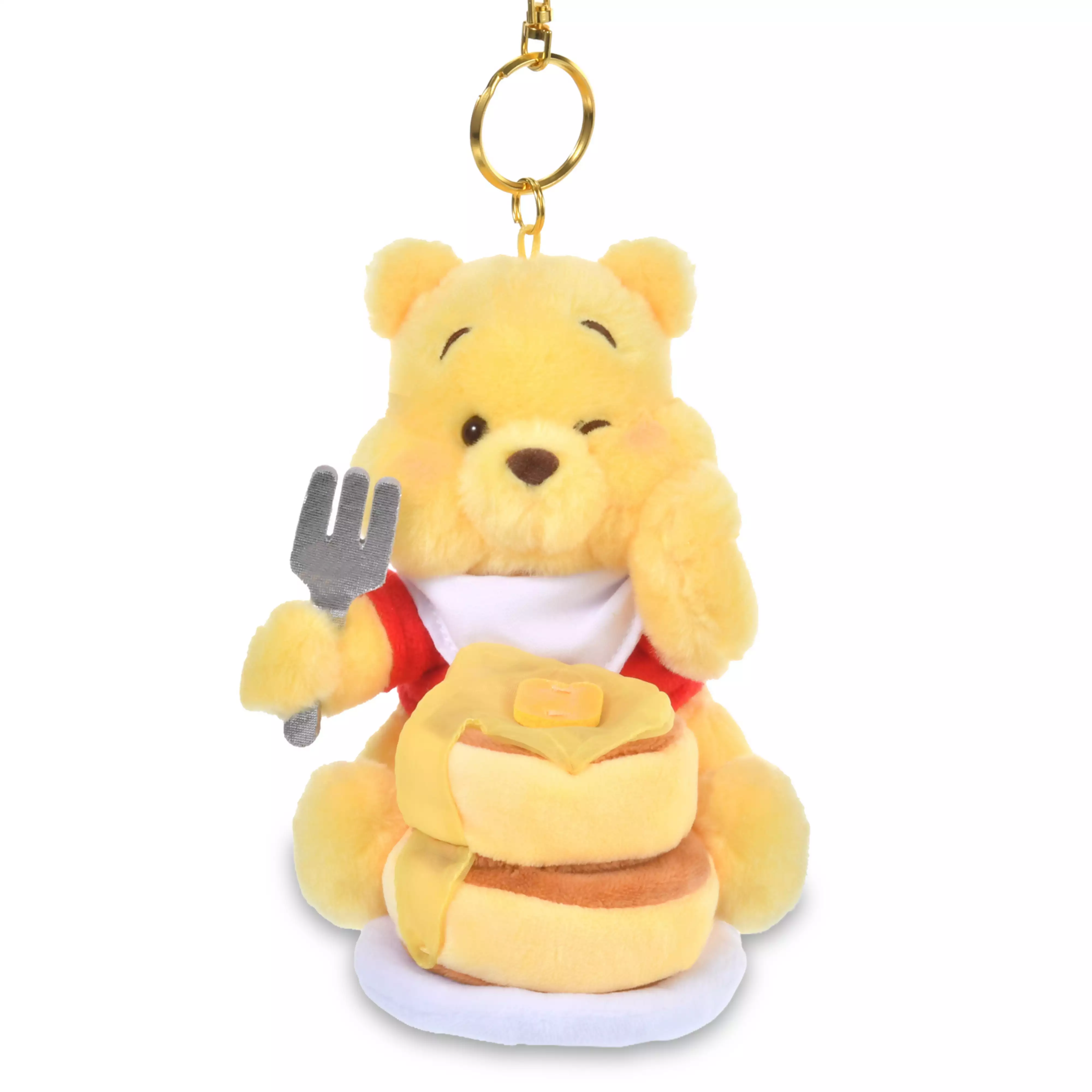 Plush Winnie the Pooh keychain holding a fork and sitting behind a stack of pancakes.