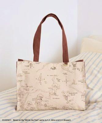 Square cotton tote bag with a light background and Winnie the Pooh sketch print and brown handles photographed on a striped surface.