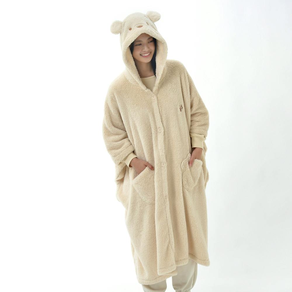 Model wearing a beige Pooh-themed wearable boa fleece blanket with a hood with bear ears and front pockets.