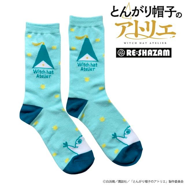 Light blue women's socks on a white background showing a triangular hat motif, "Witch hat Atelier" text, yellow star dots, and teal toes.