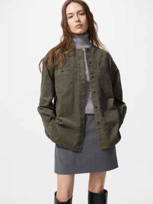 A model wearing the corduroy long shirt jacket over a gray turtleneck and skirt, shown from the front.
