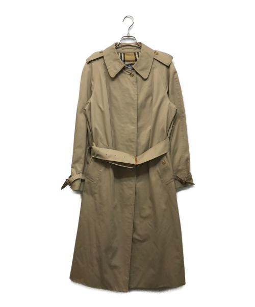 Beige women's cotton ステンカラーコート hanging on a hanger against a white background.