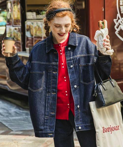 Model wearing the women's denim jacket (Gジャン) shown front-facing, holding a coffee cup and a sandwich while carrying a tote bag.