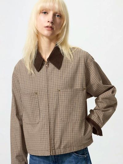 A woman wearing a short zip-up cotton jacket with a dark contrast collar and a small checked pattern.