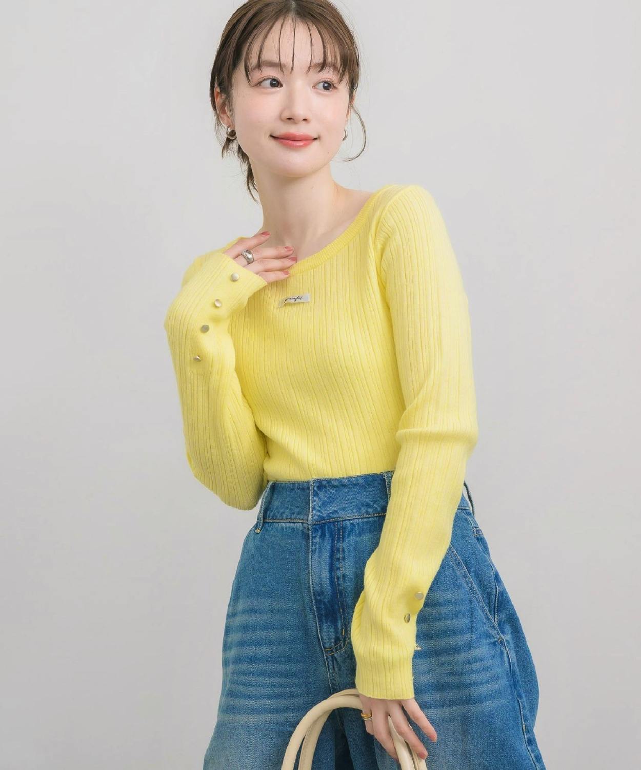 Model wearing a yellow crew-neck rib knit top with long sleeves paired with blue jeans.