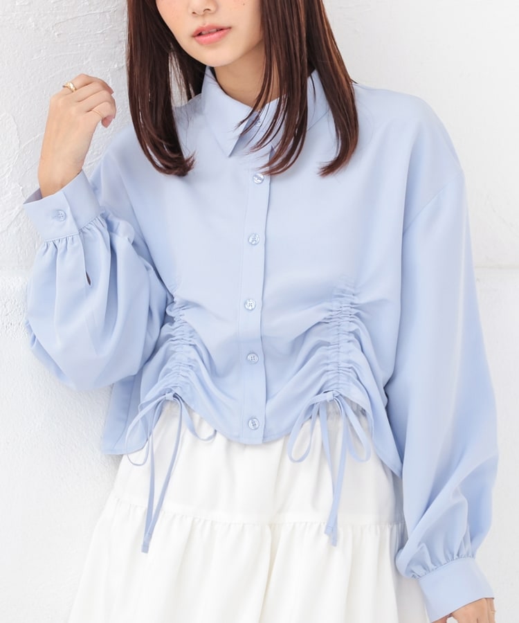Model wearing a light blue short-length drawstring button-up shirt with long puff sleeves and front ruched ties.