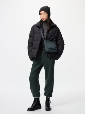 Woman wearing dark green fleece easy pants styled with a black puffer jacket and beanie against a white background.