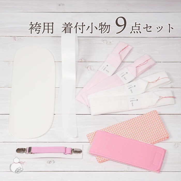 Nine-piece hakama kimono dressing accessory set laid flat, showing a front board, datejime, eri-shin, belts, and four waist cords in white and pink.