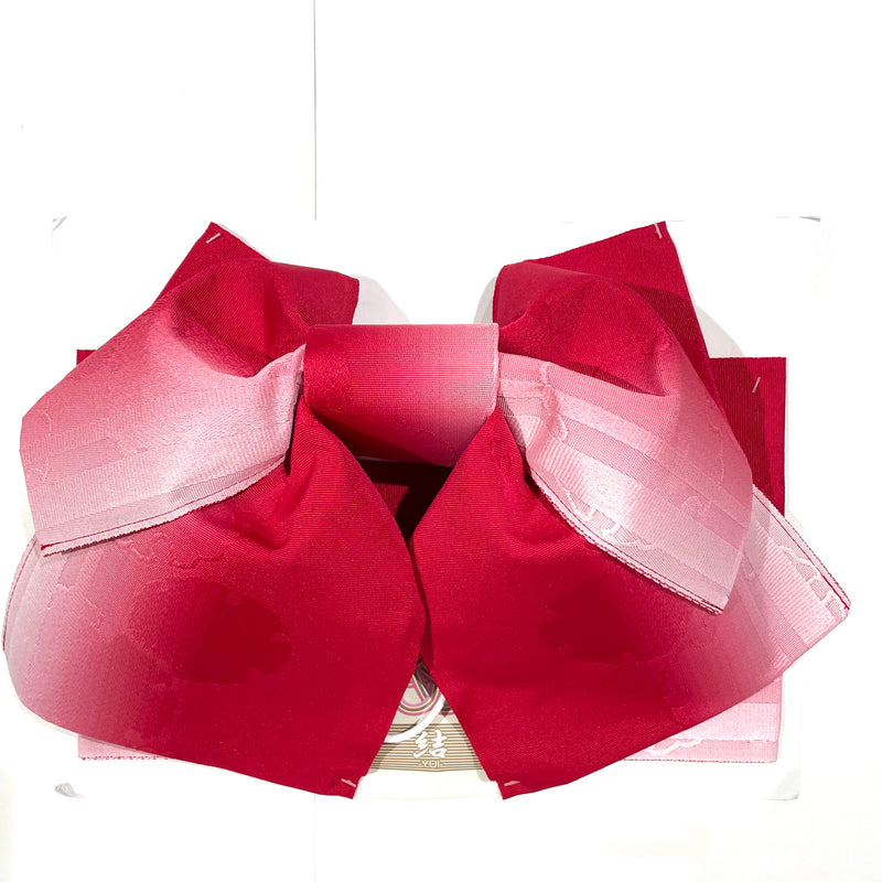 Red to pink ombré women's hanhaba obi tied in a decorative bow on a white background.
