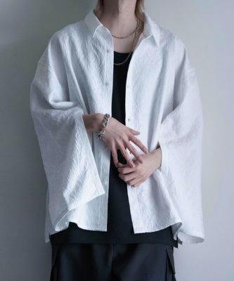 Model wearing a white long-sleeved women's shirt over a black top, shown from neck to hips.