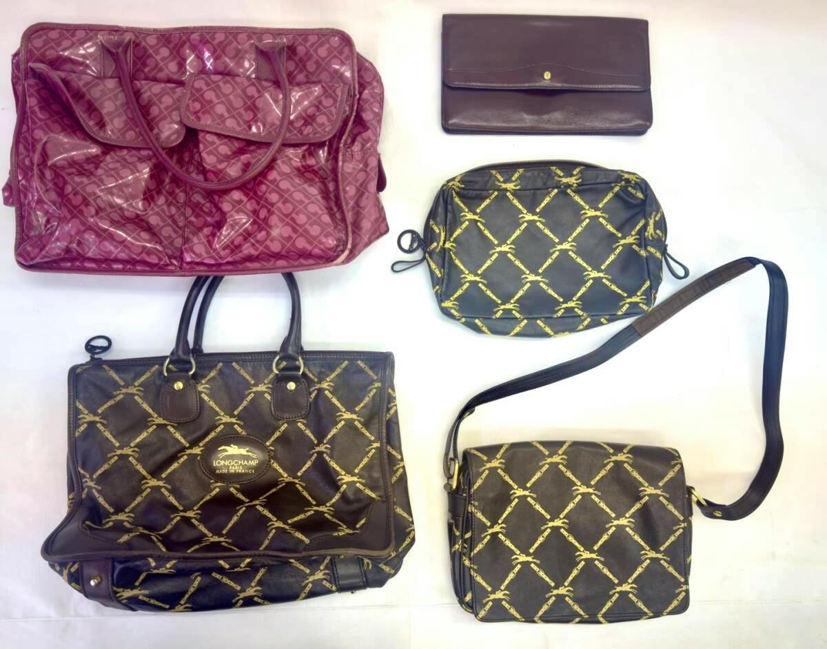 Five women's bags on a white background: a pink tote, a Longchamp patterned tote, a Longchamp patterned shoulder bag with strap, a small pouch, and a brown clutch.