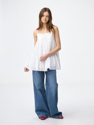 Model wearing a white camisole tunic over wide-leg jeans against a plain background.