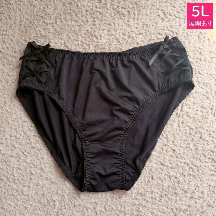 Black women's polyester underwear with crisscross ribbon details at the sides laid flat on a textured background.