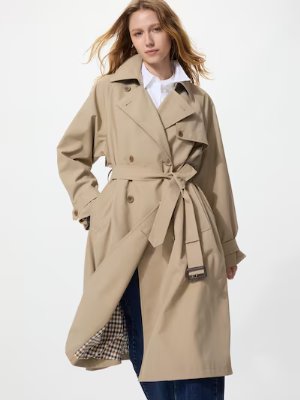 Woman wearing a beige relaxed-fit trench coat with a waist tie belt and double-breasted front.