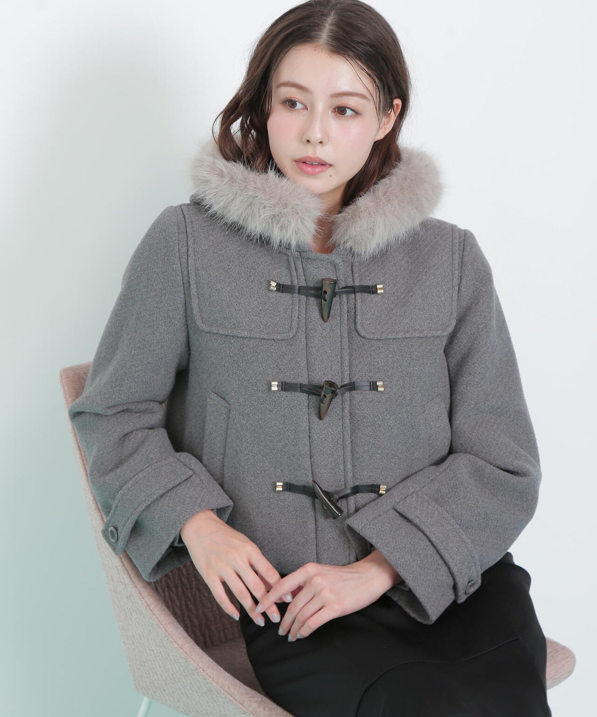 Model wearing a grey short duffle coat with faux-fur collar and toggle closures.