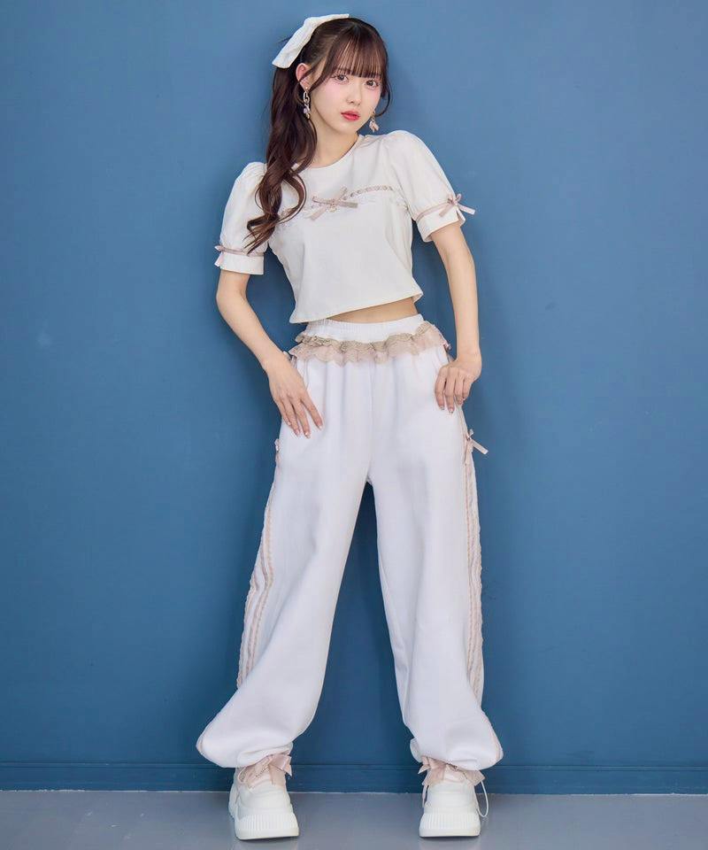 Model wearing the women's side-lace design sweatpants in white, standing against a blue wall.