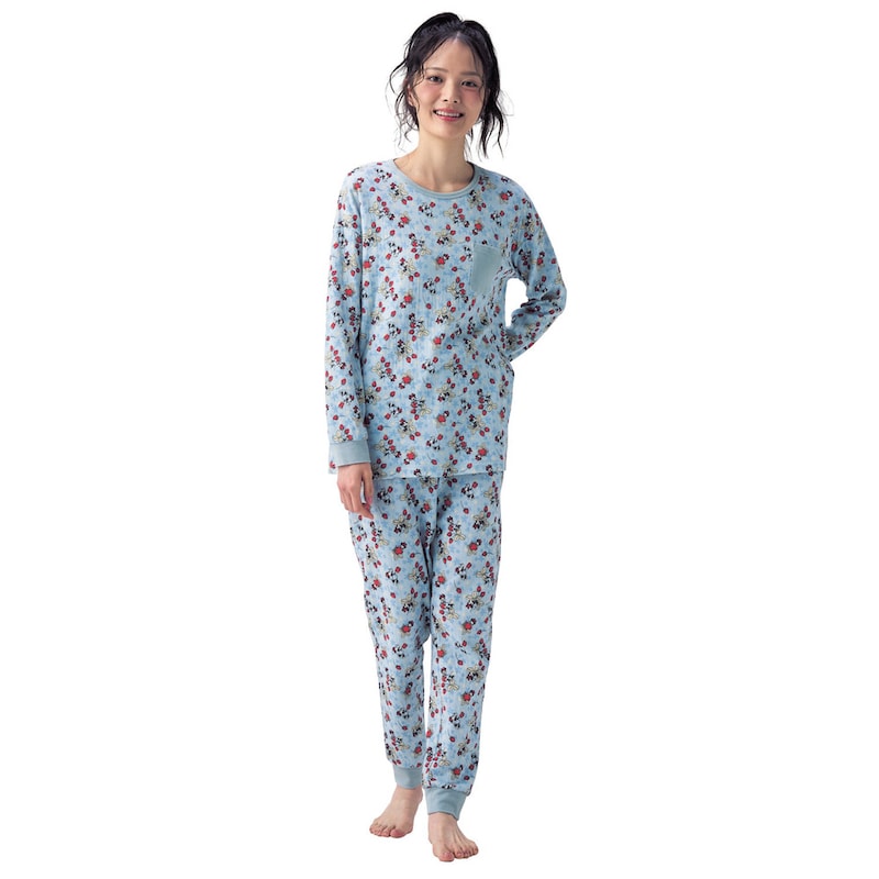 A woman wearing a light-blue long-sleeve women's cotton pajama set with an all-over pattern, standing barefoot and smiling.