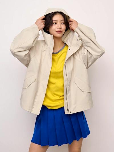 Woman wearing a beige women's utility parka (polyester) adjusting the hood, shown from the front.