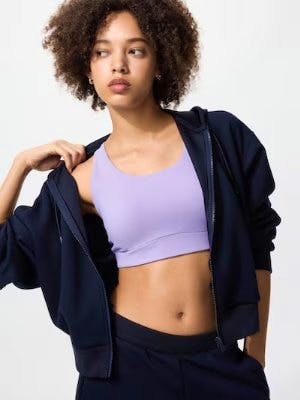 Model wearing a lavender wireless U-neck bra under a navy zip-up hoodie.