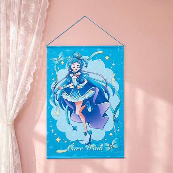 A B2 tapestry featuring the character Cure Wink hanging on a pink wall beside a lace curtain.
