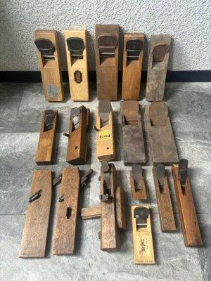Multiple wooden hand planes of various sizes arranged on a tiled floor against a wall.
