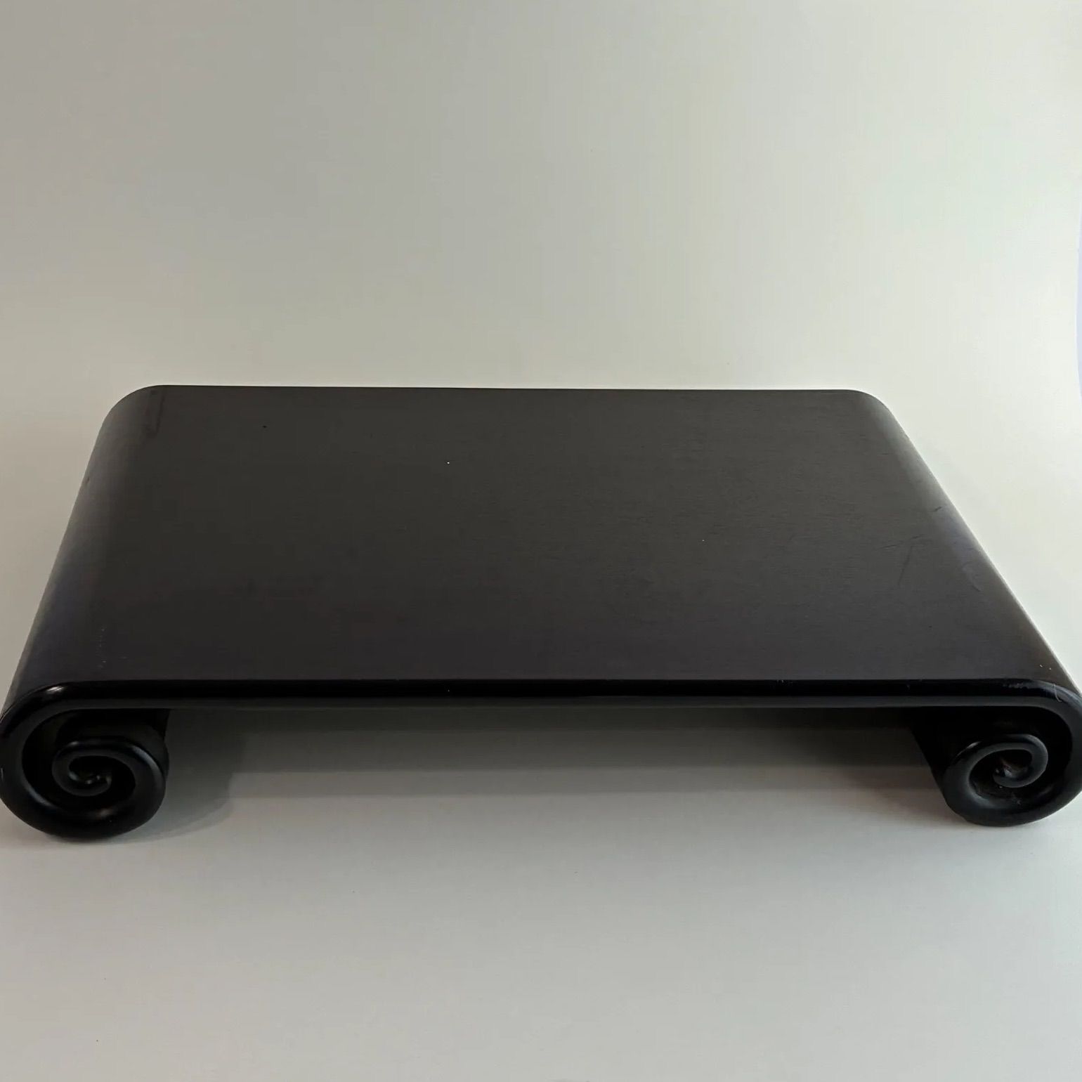 Black wooden display stand with rolled, scroll-like legs photographed on a white background.