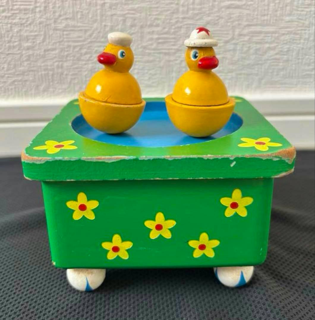 Wooden green music box with two yellow duck figures on top and painted flower decorations.