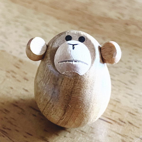 A small wooden monkey roly-poly ornament photographed on a wooden surface.