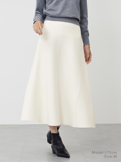 A model wearing a cream white wool-cotton blend flared women's skirt paired with a grey sweater and ankle boots.