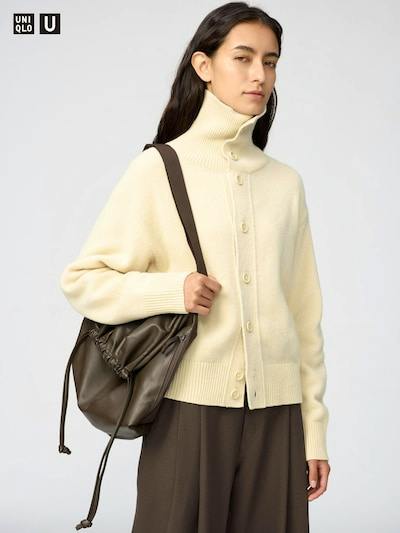 Model wearing a cream stand-collar wool cardigan buttoned at the front and carrying a shoulder bag.
