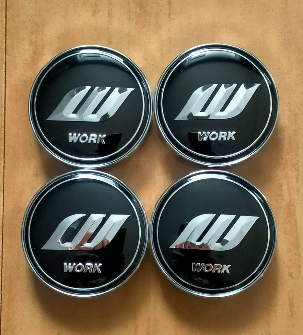 Four WORK wheel center caps with black faces and silver WORK logo arranged on a wooden surface.