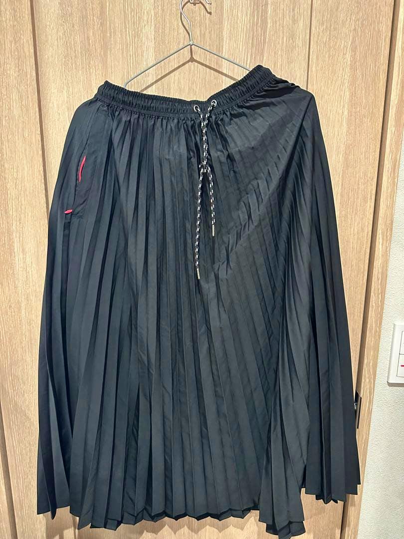 Black pleated skirt with an elastic drawstring waistband hanging on a hanger against a wooden background.