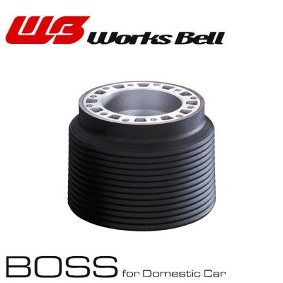 Photo of a Works Bell steering boss showing a black ridged cylindrical boss with a silver top ring and the Works Bell logo above.