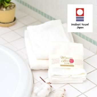 Folded white mini bath towels on a tiled bathroom surface beside a sink, with a product label and a small brand logo overlay.