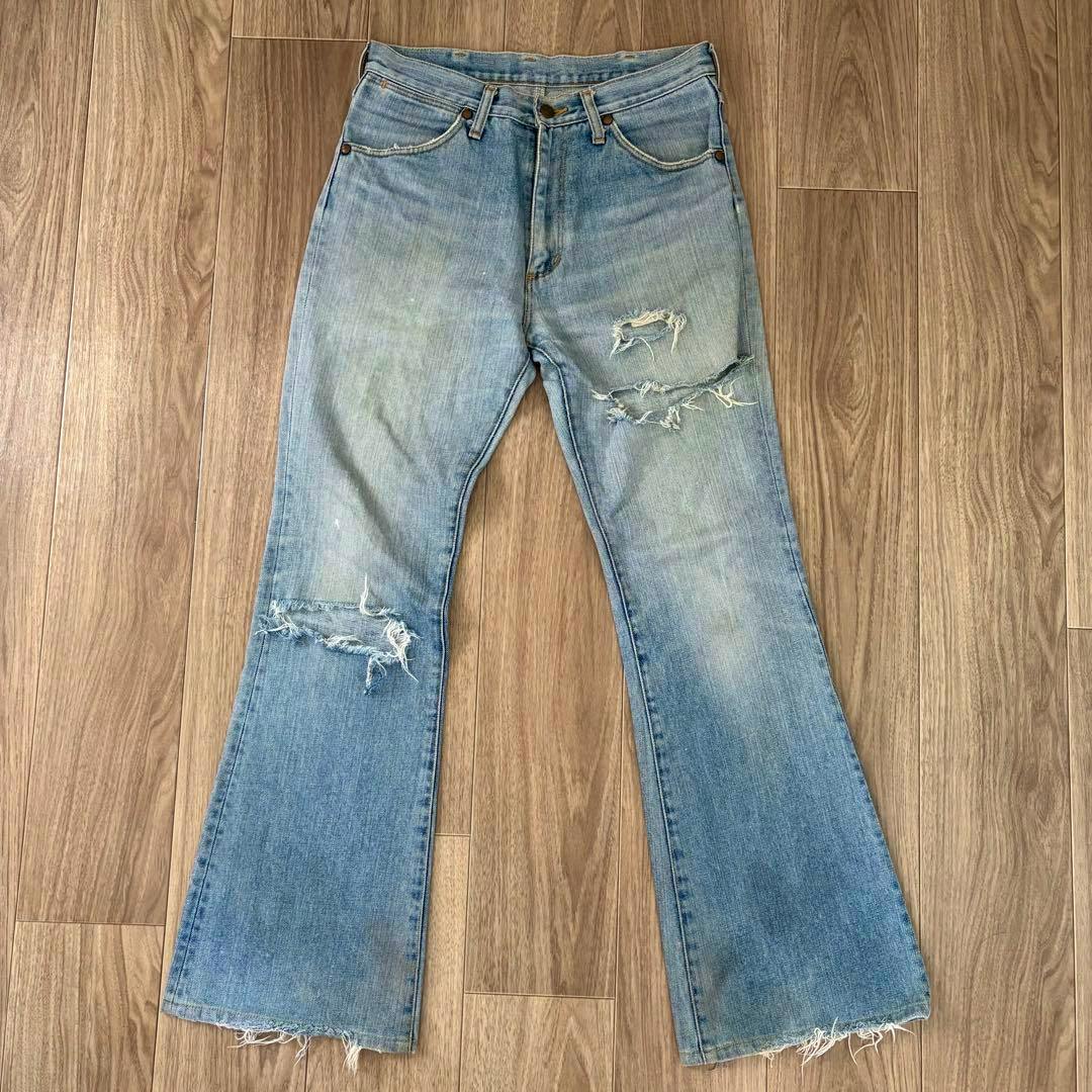 Front view of men's Wrangler bootcut denim jeans laid flat showing distressed knees and frayed hems.