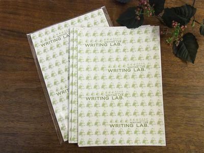 Stacked WRITING LAB. absorbent writing paper pads with a green repeating logo on a wooden tabletop.