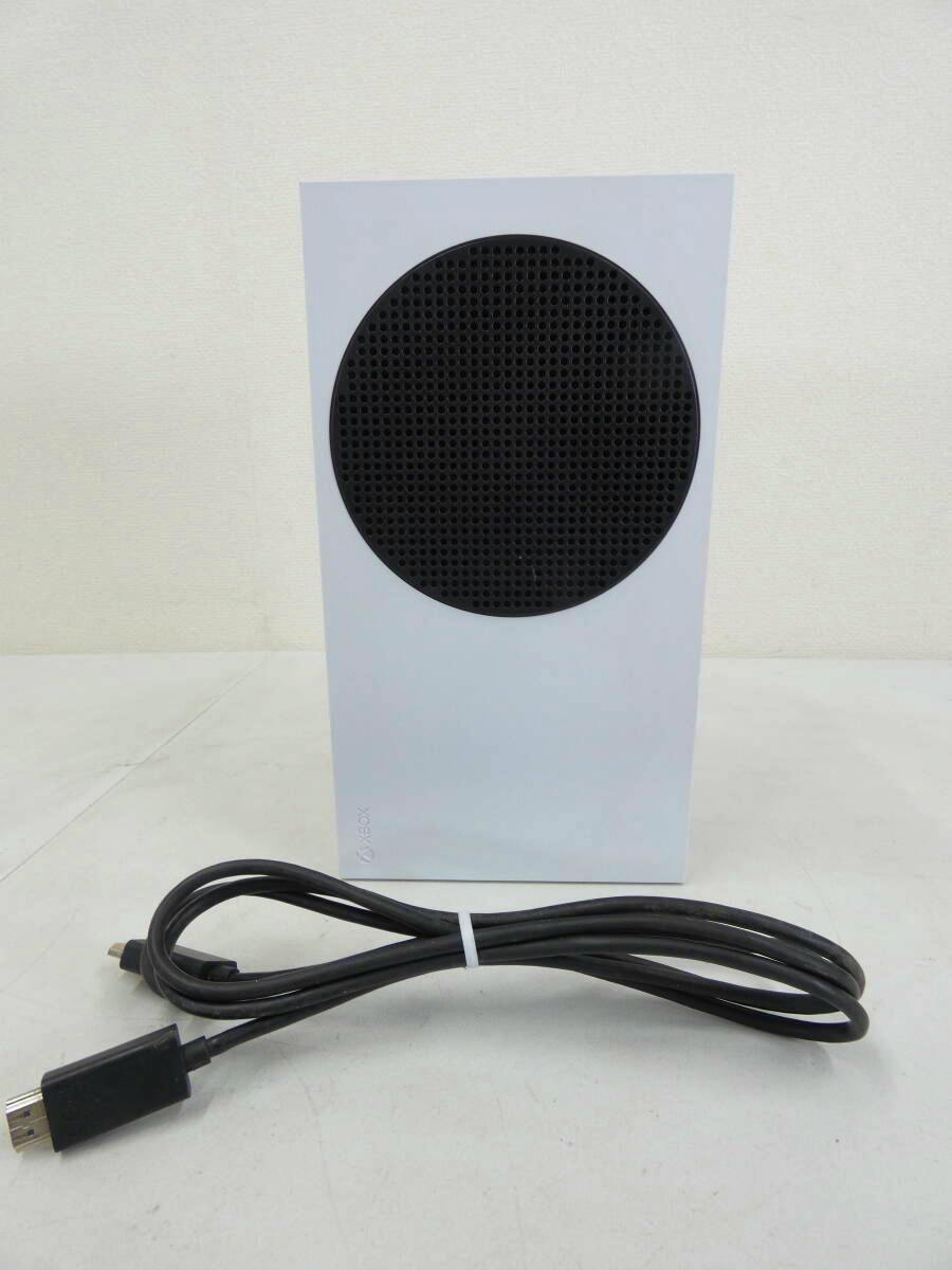 White Xbox Series S console standing upright with its black circular vent visible and a coiled HDMI cable placed in front.