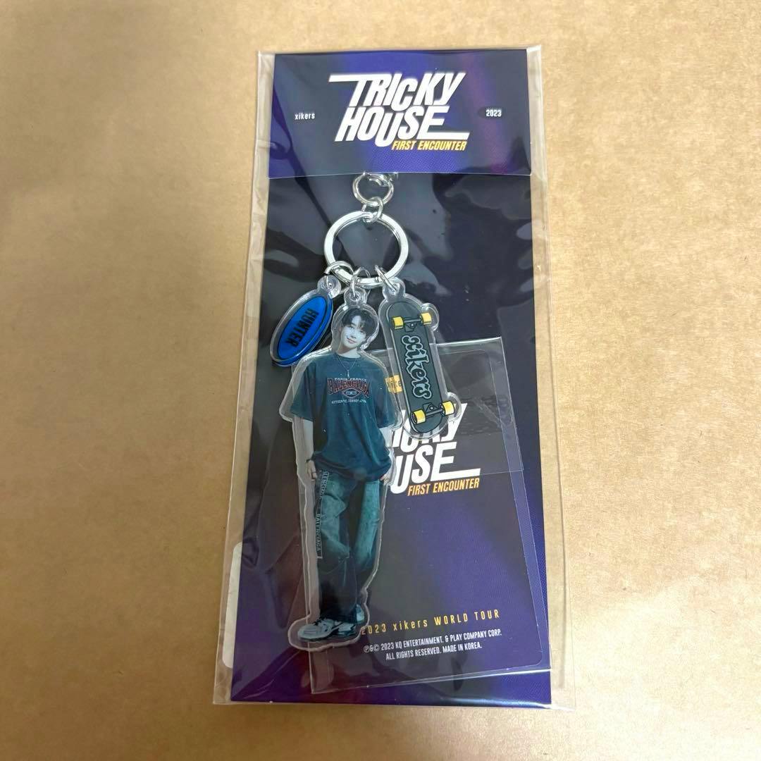 Packaged acrylic keychain featuring a full-body character charm, skateboard charm, and oval tag on a purple "Tricky House" backing card.