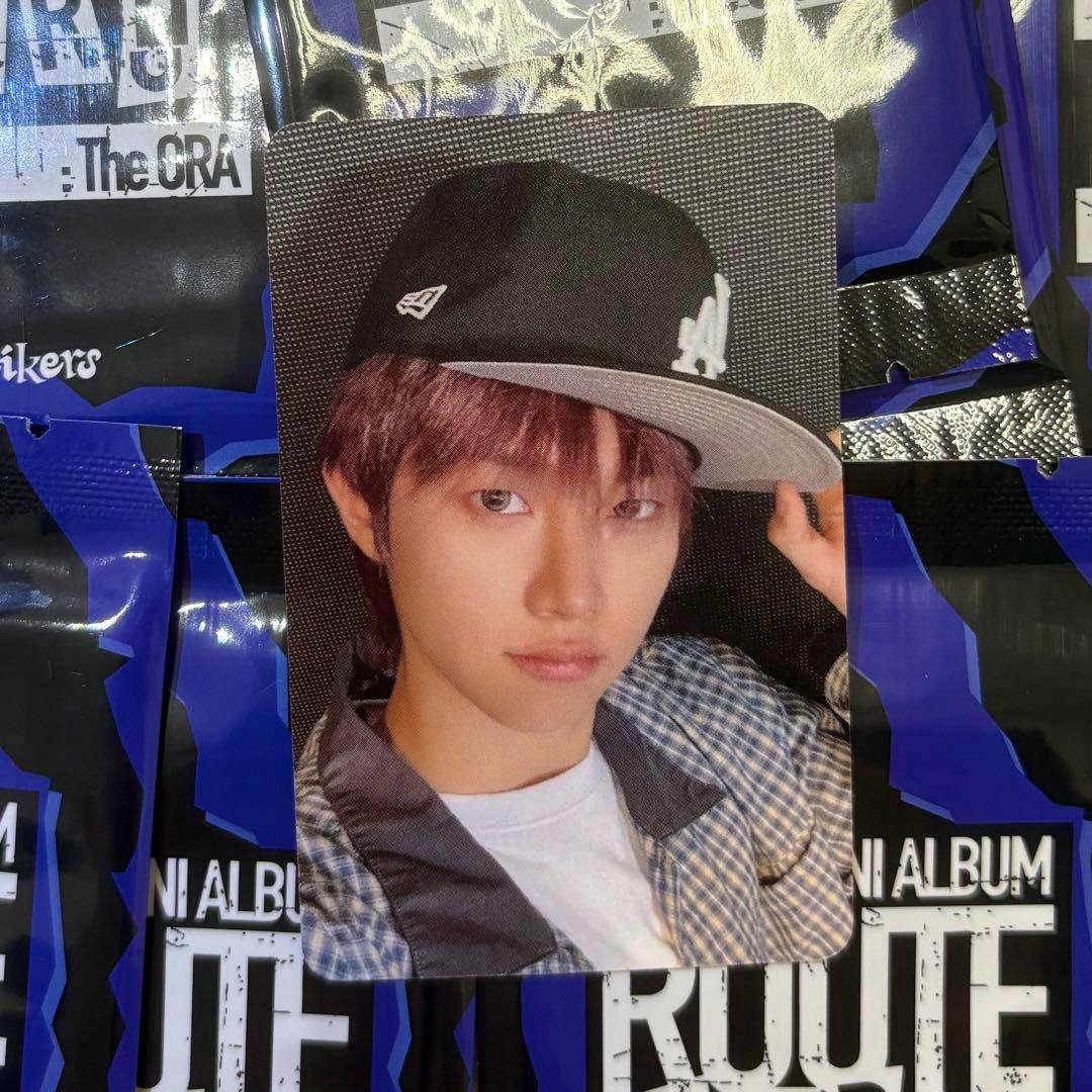 Front side of the photocard showing a close-up portrait of the card subject wearing a baseball cap placed on top of purple album packaging.