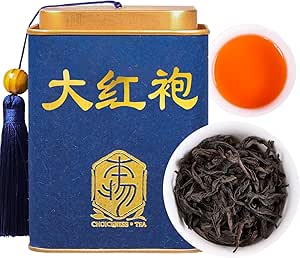 Blue tea tin labeled "Da Hong Pao" with a tassel, shown alongside a bowl of loose tea leaves and a cup of amber brewed tea.