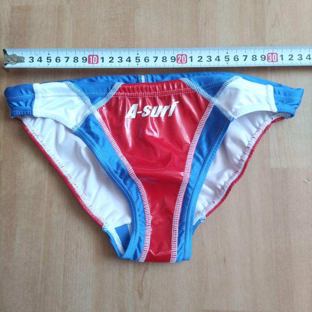 XL men's enamel racing swim brief in red, blue, and white laid flat with a measuring tape above.