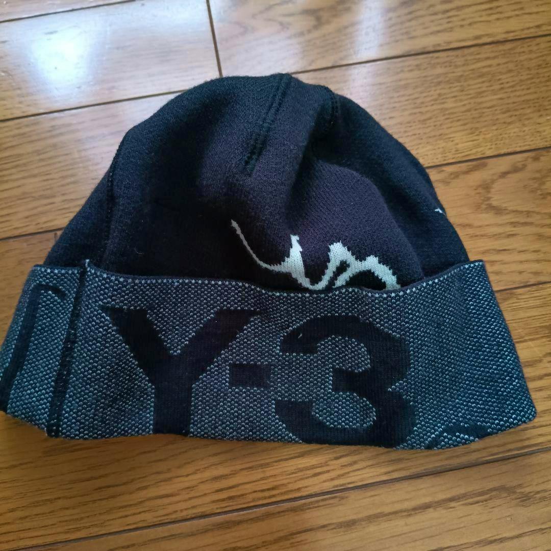 Black Y-3 knit beanie with a folded patterned cuff showing the Y-3 logo, laid on a wooden floor.