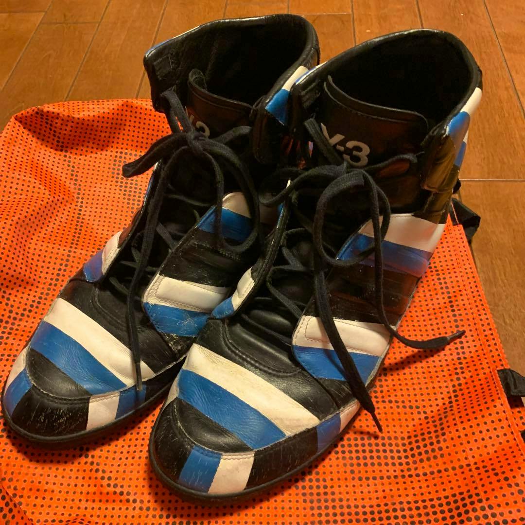 Pair of Y-3 leather sneakers with blue, white, and black stripes placed on an orange dotted surface.