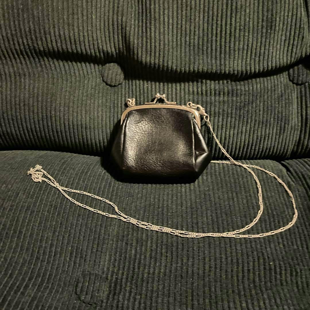 Black cow leather がま口 wallet with a long silver chain placed on a dark ribbed couch.