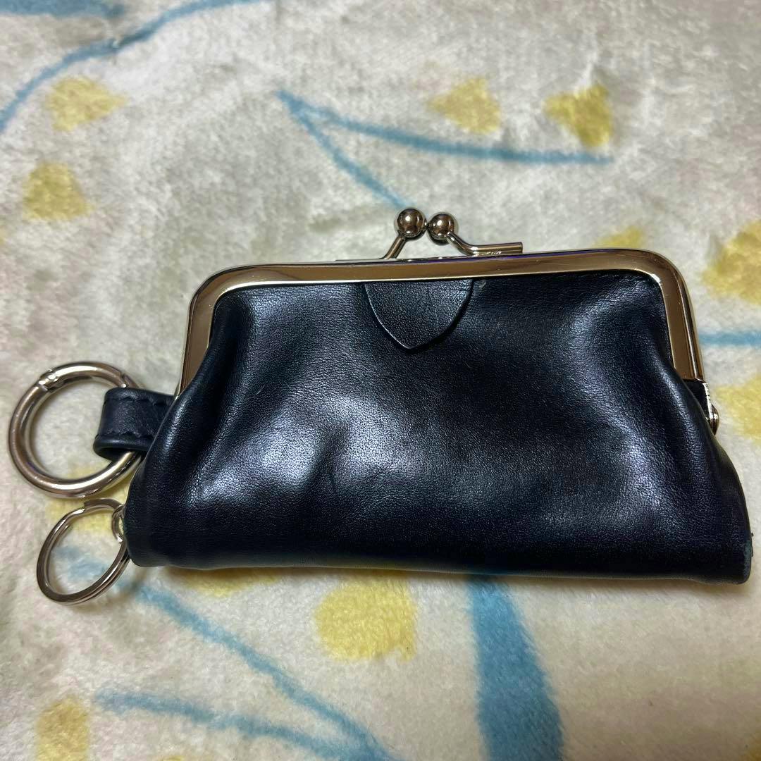 Black leather kiss-lock coin purse with a metal frame and two attached key rings on a patterned blanket.
