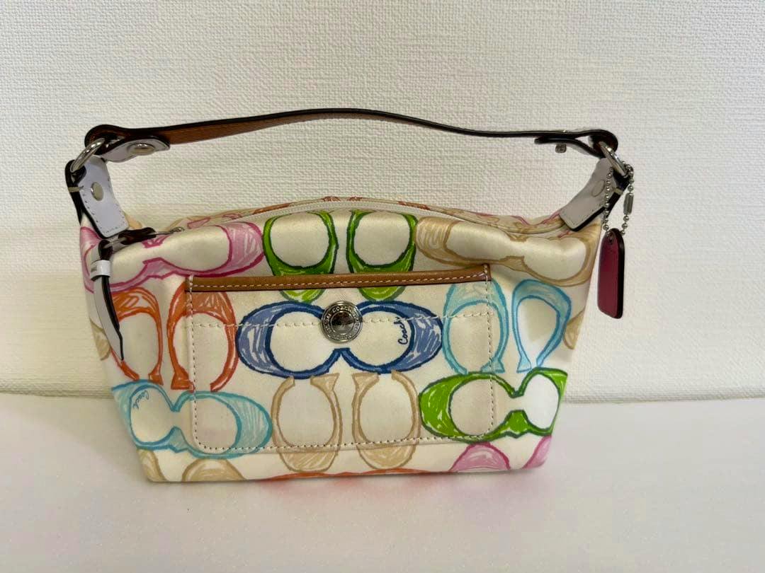 A small Coach canvas handbag with a multicolored C pattern, short leather handle, and a metal button on the front pocket.